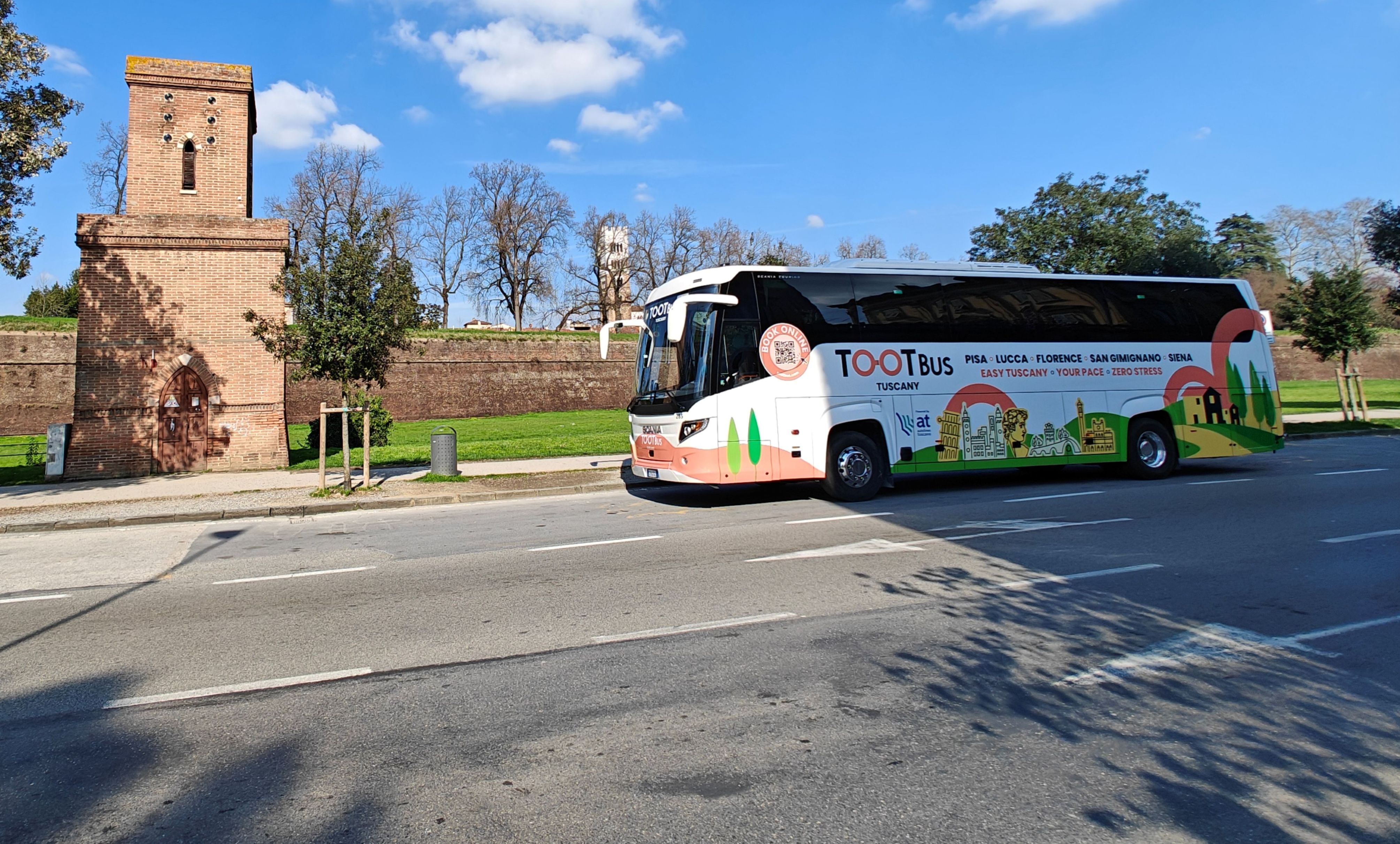 Tootbus coach parked in front of the medieval walls and a brick tower in Lucca, Italy.