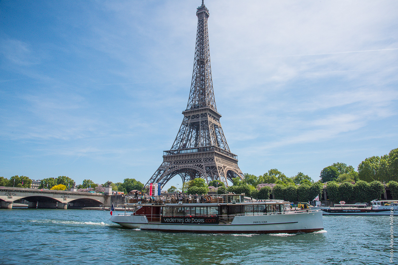 Un barco de crucero de Vedettes de Paris navegando por el río Sena con la Torre Eiffel al fondo.
