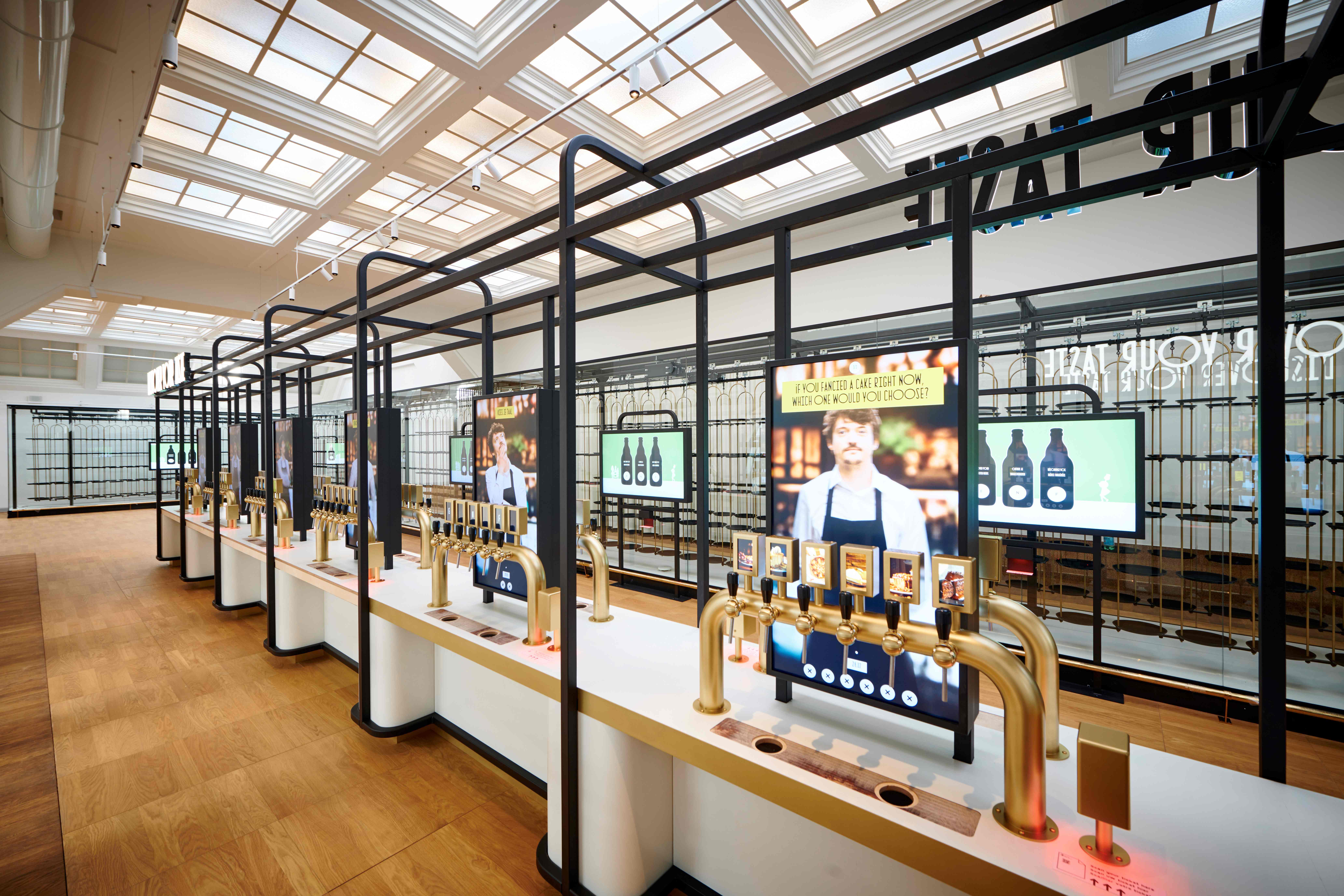 La sala de degustación interactiva del museo Belgian Beer World en la Bolsa de Bruselas, equipada con mostradores largos con grifos de cerveza dorados y pantallas digitales bajo un gran techo de cristal.