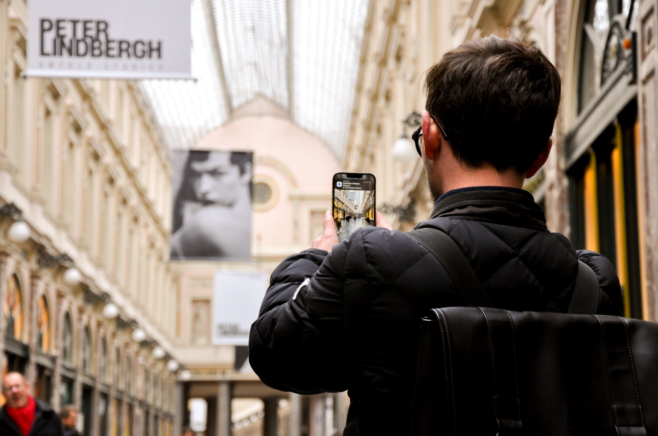 Een man van achteren fotografeert met zijn smartphone de Koninklijke Sint-Hubertusgalerijen in Brussel.