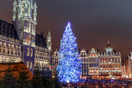 Blik over de schouder van een persoon die met hun smartphone een foto maakt van het verlichte reuzenrad en de feestelijke kerstbus van Tootbus, 's nachts in Brussel.