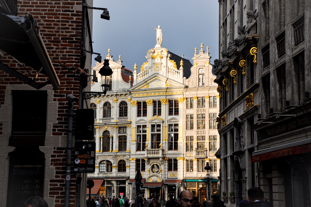 View from a narrow street looking onto the golden facades of the Brussels Grand-Place.