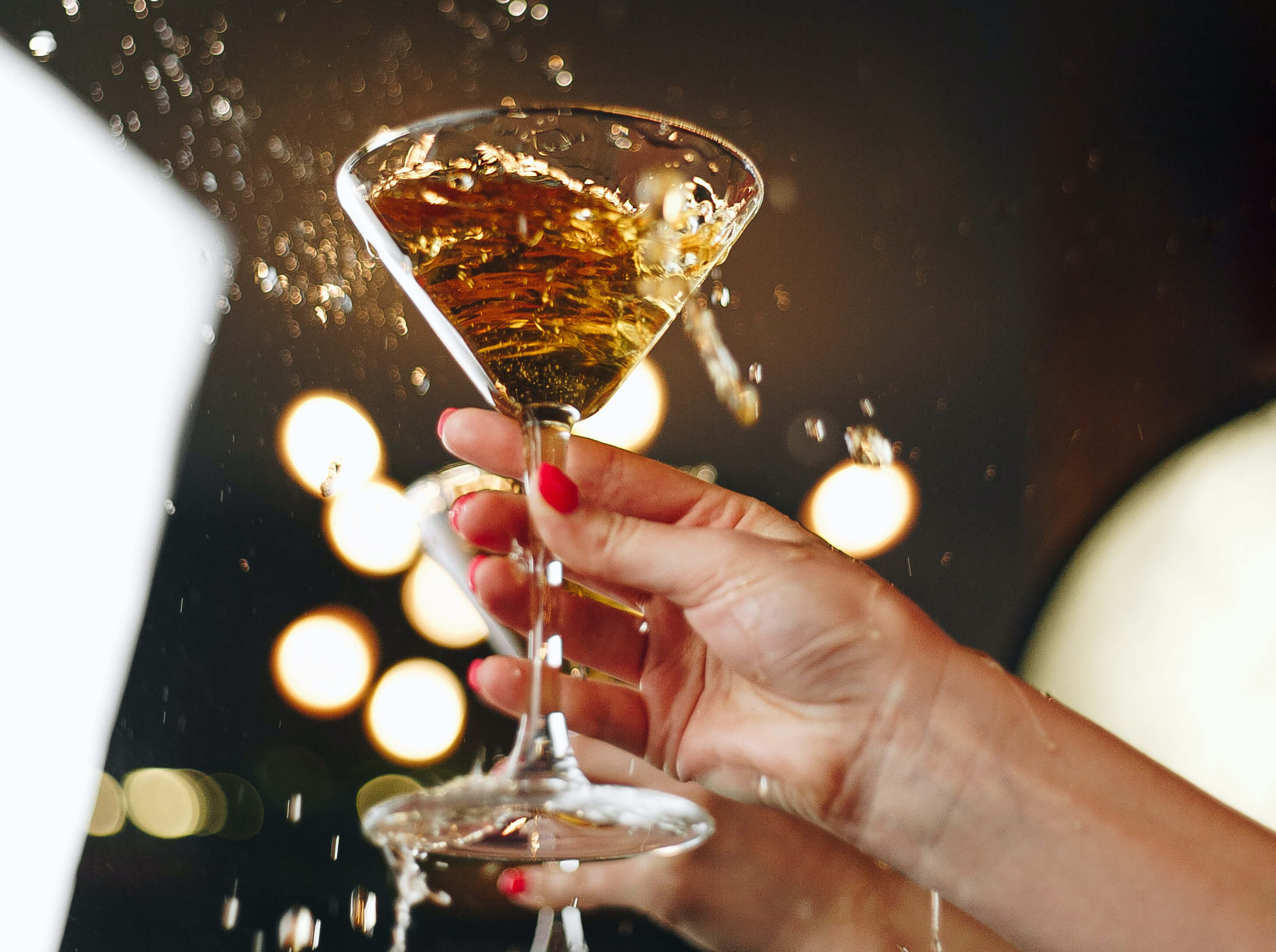 Hand die een bewegend cocktailglas vasthoudt met spatten tijdens het uitgaan.