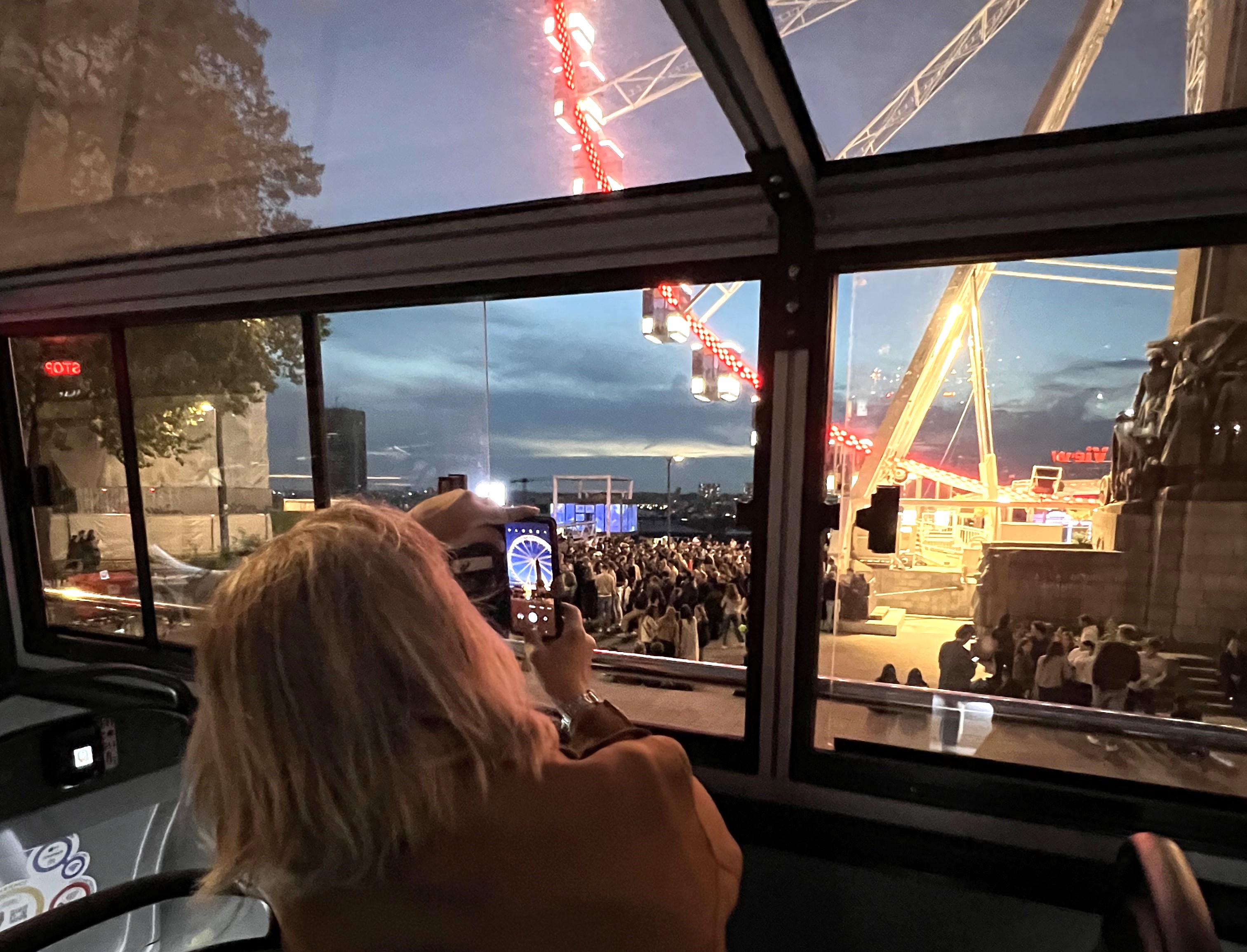 A woman inside a Tootbus takes a night photo of the illuminated Ferris wheel on Place Poelaert.