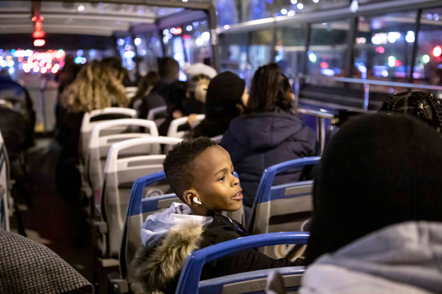 Blik over de schouder van een persoon die met hun smartphone een foto maakt van het verlichte reuzenrad en de feestelijke kerstbus van Tootbus, 's nachts in Brussel.
