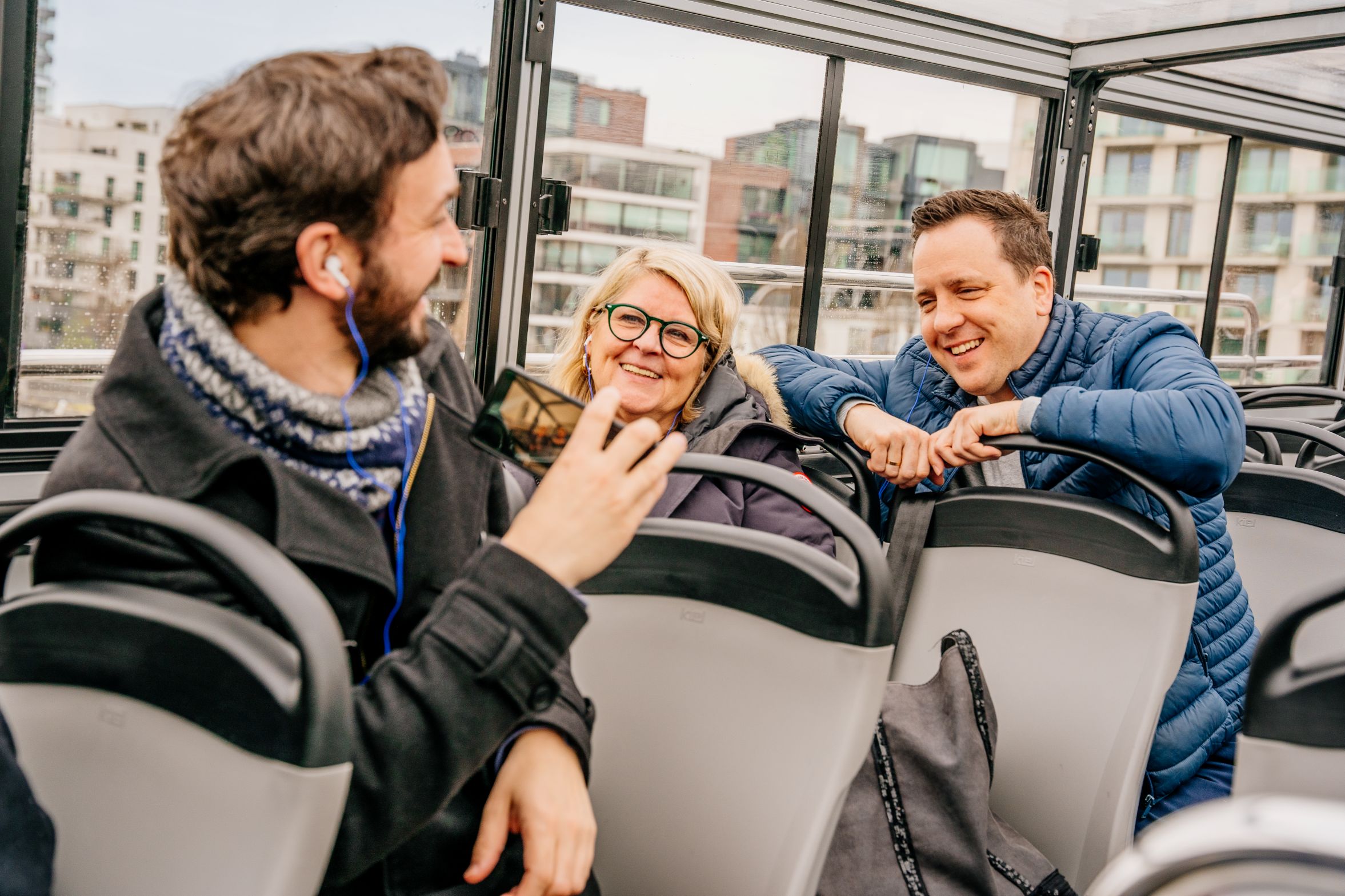 Passagiers op het open bovendek van een Tootbus Brussels die aankomen op het Koningsplein, met de Sint-Jacob-op-Coudenbergkerk en het standbeeld van Godfried van Bouillon op de achtergrond.