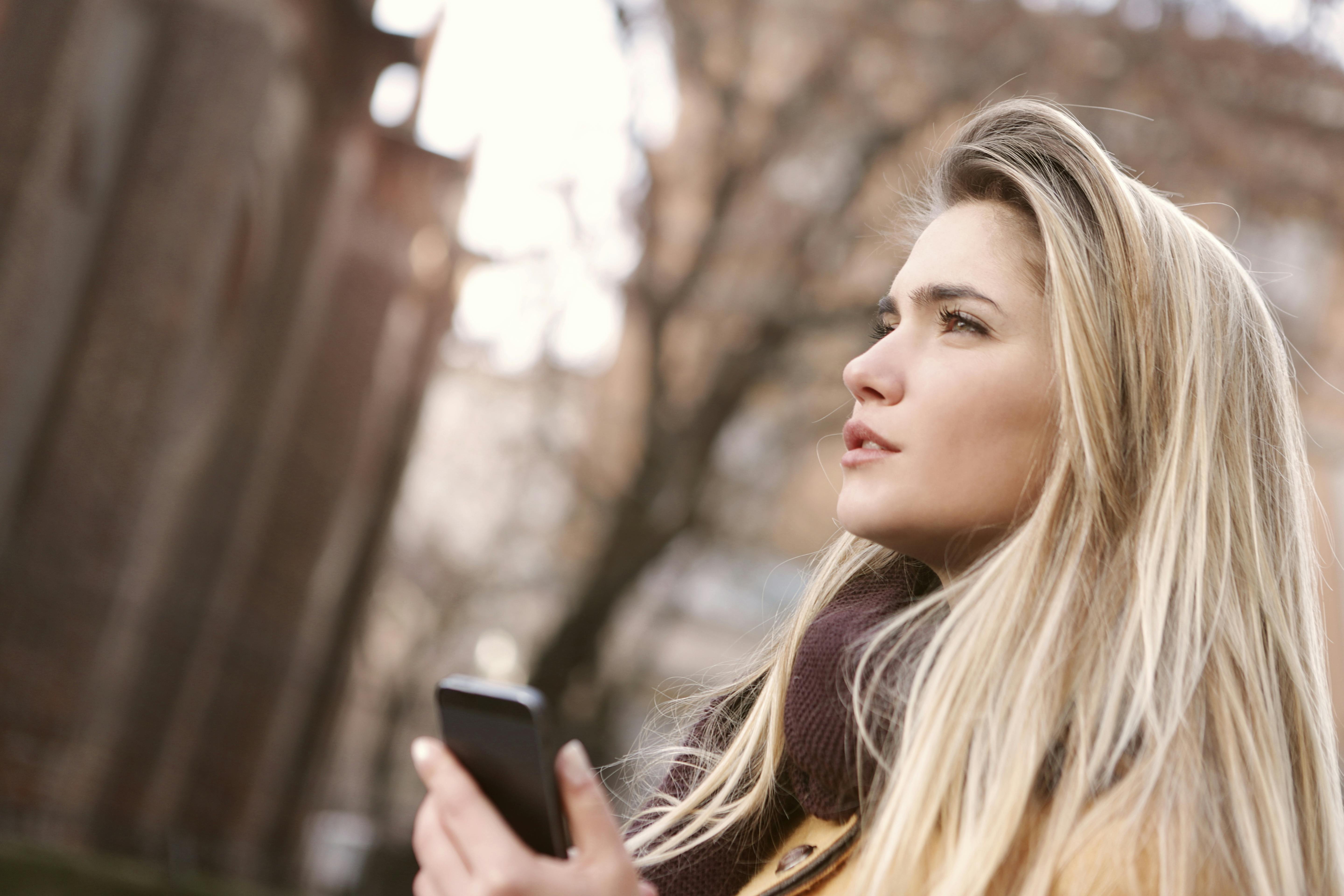 Profile of a young blonde woman holding her smartphone in the street during the Emily in Paris tour.