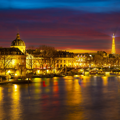 Vue nocturne de la Seine à Paris avec les reflets dorés des monuments illuminés, l'Institut de France à gauche et la Tour Eiffel au loin.