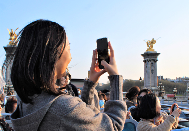 Split image showing on the left the Pont Neuf in Paris during the day and on the right the illuminated Institut de France at night reflecting on the Seine river.