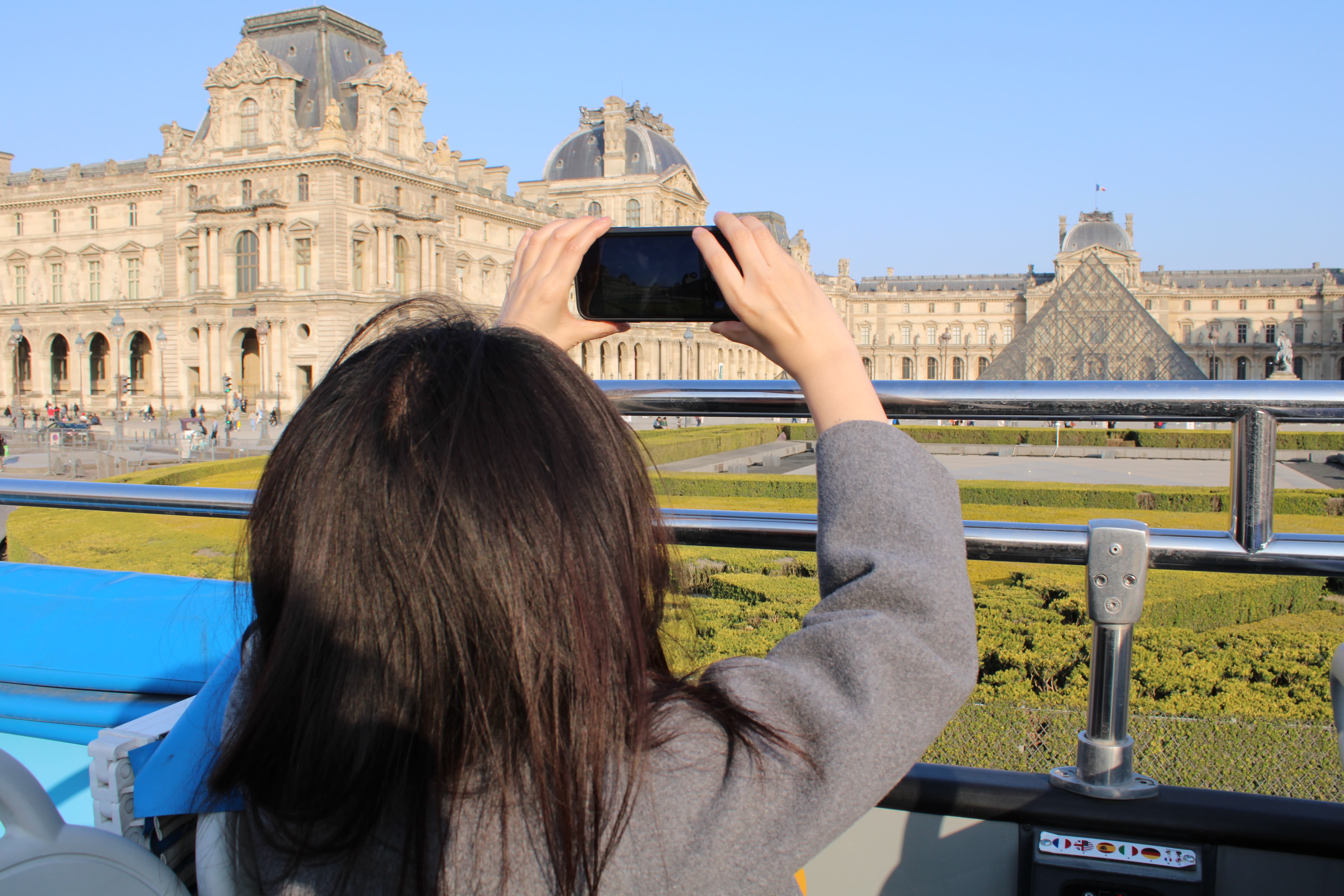 Una pasajera de espalda a bordo de un Tootbus toma una foto del Museo del Louvre con su teléfono inteligente.
