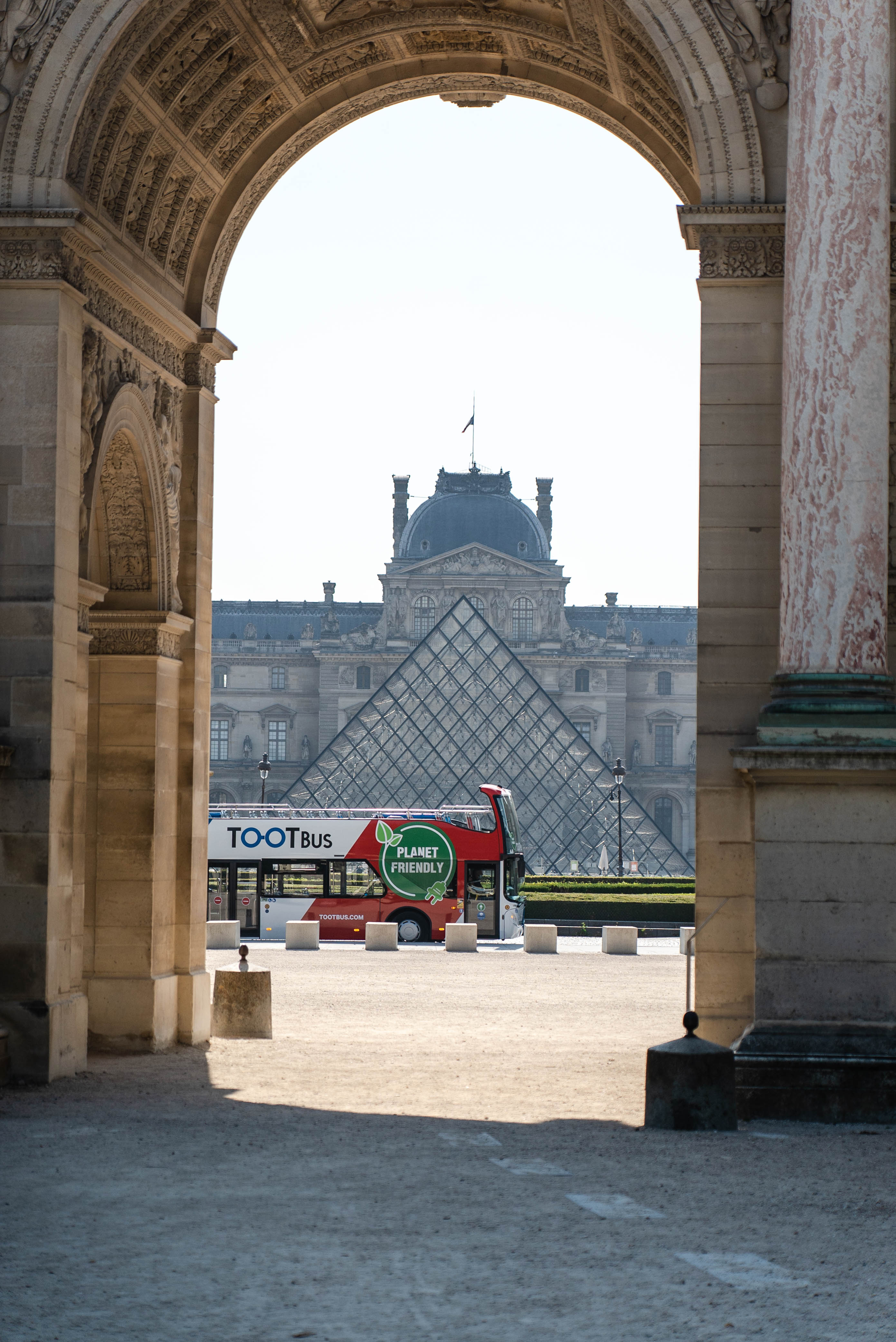 View through the Carrousel archway of a Tootbus driving past the Louvre pyramid.