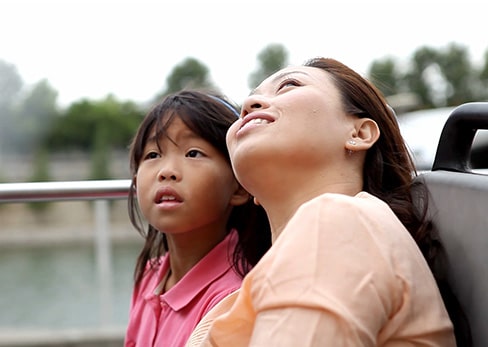 A mother and daughter look up with wonder from the open top deck of a Tootbus.