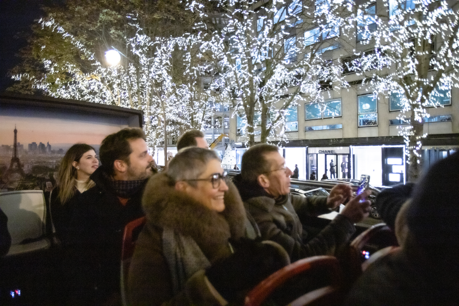 Pasajeros abrigados admiran las luces de Navidad blancas en los árboles de los Campos Elíseos desde el piso superior de un autobús Tootbus durante una ruta privada nocturna.