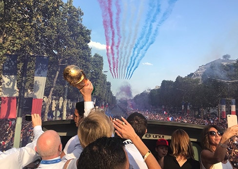 Vista desde el piso superior de un Tootbus privado en los Campos Elíseos abarrotados de gente, con el trofeo de la Copa del Mundo en alto y la Patrouille de France volando con humo tricolor.