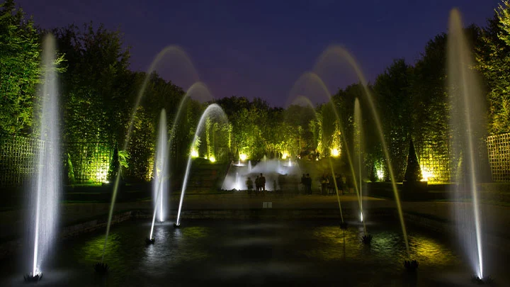 Los chorros de agua iluminados del bosquet de la Sala de Baile se elevan en forma de arco por la noche durante las Grandes Aguas Nocturnas de Versalles.
