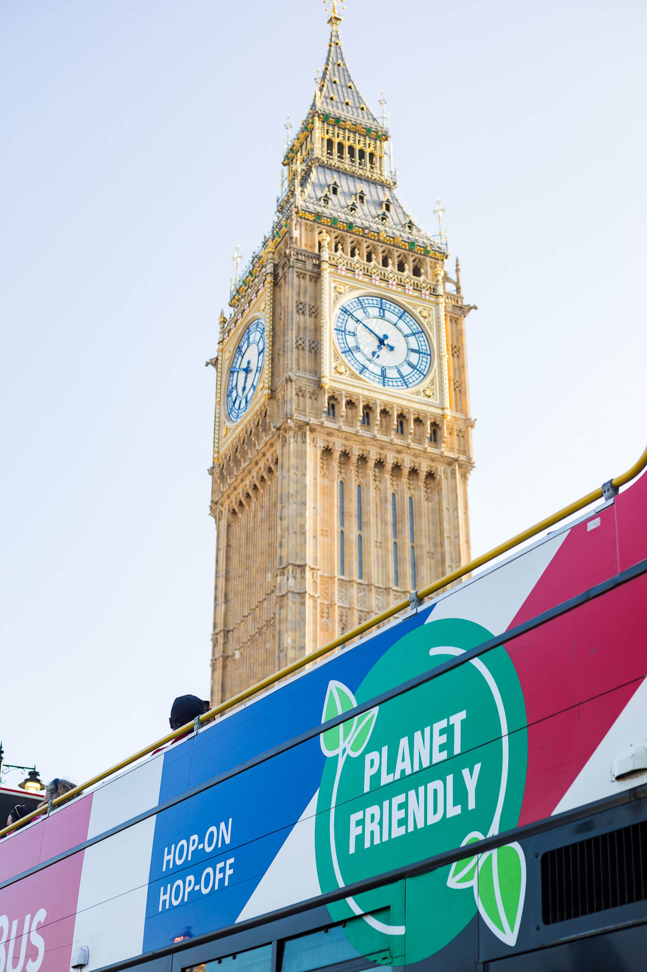 Gros plan sur le côté d'un bus Tootbus affichant le logo "Planet Friendly", avec la tour de l'horloge du Big Ben s'élevant en arrière-plan à Londres.
