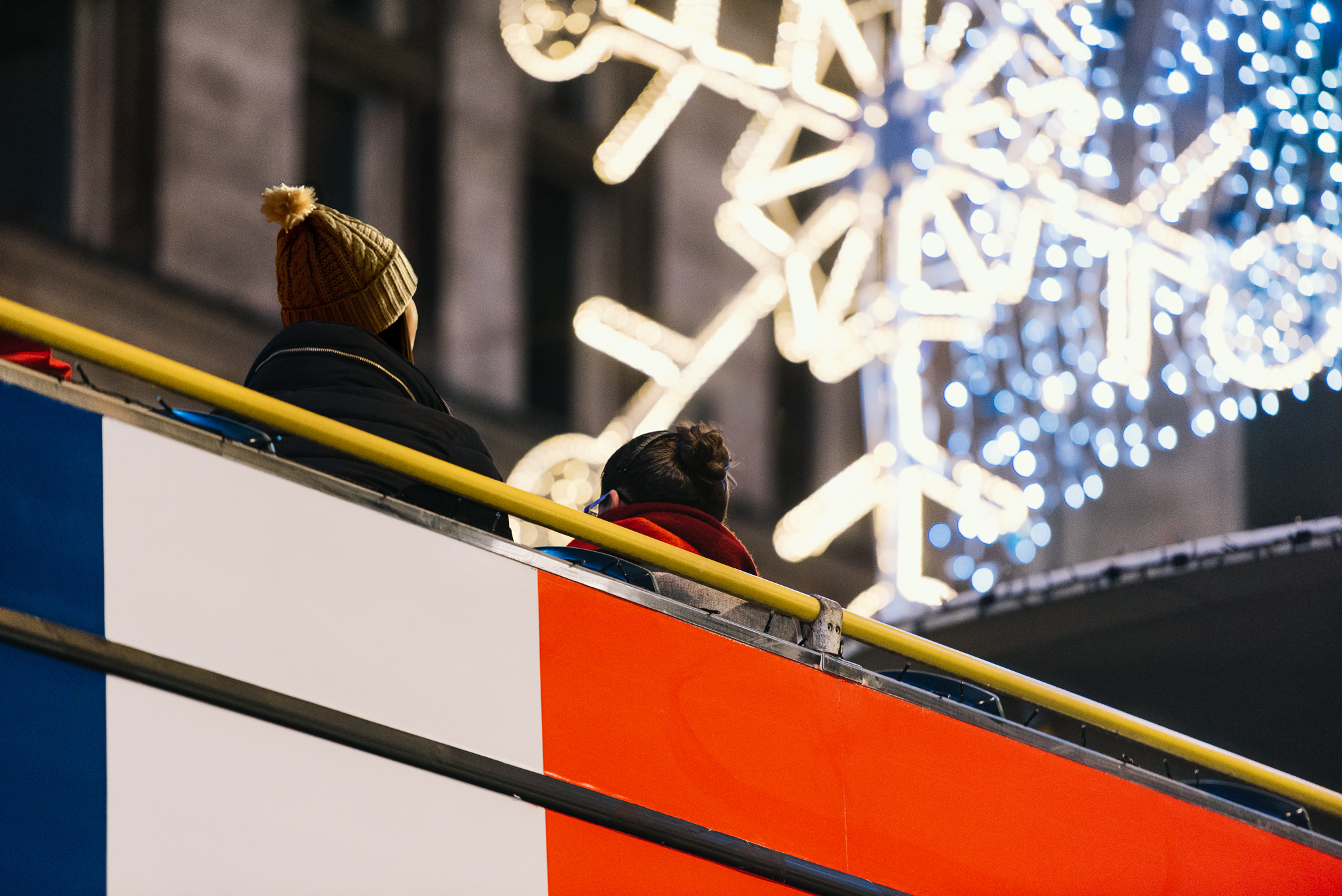 Vista en contrapicado de pasajeros con ropa de invierno en el piso superior de un Tootbus, admirando las luces de Navidad en forma de copo de nieve en Londres.
