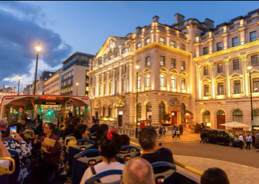 Des passagers assis à l'étage supérieur d'un bus décapotable Tootbus lors d'un tour de nuit à Londres, admirant de magnifiques bâtiments classiques illuminés.