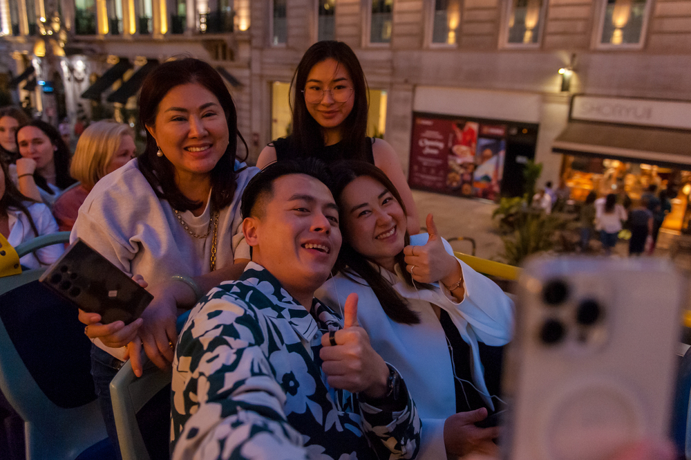 Un groupe d'amis souriants prenant un selfie et faisant un pouce levé à l'étage supérieur d'un bus décapotable Tootbus lors d'un tour de nuit à Londres.