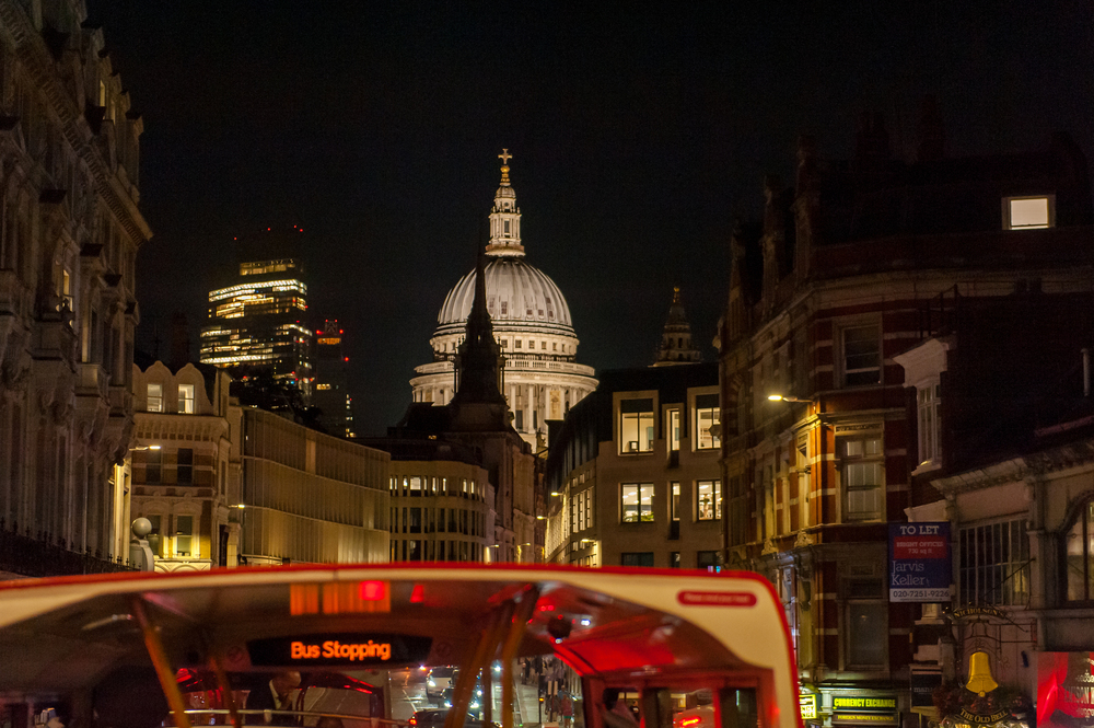Vue nocturne depuis l'étage supérieur d'un bus décapotable approchant de la cathédrale Saint-Paul illuminée au bout d'une rue à Londres.