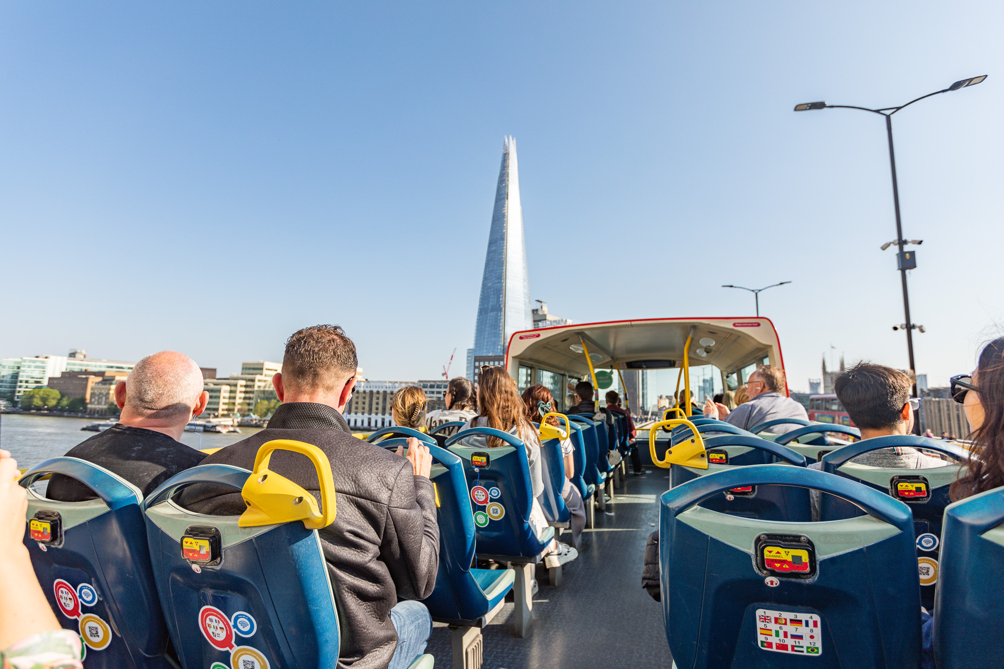 Vue depuis l'arrière de passagers assis à l'étage supérieur d'un bus décapotable à Londres, regardant le gratte-ciel The Shard au loin sous un ciel bleu.