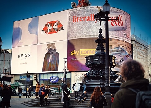 Vue des célèbres écrans publicitaires géants et de la fontaine d'Eros à Piccadilly Circus à Londres, avec des passants au premier plan.