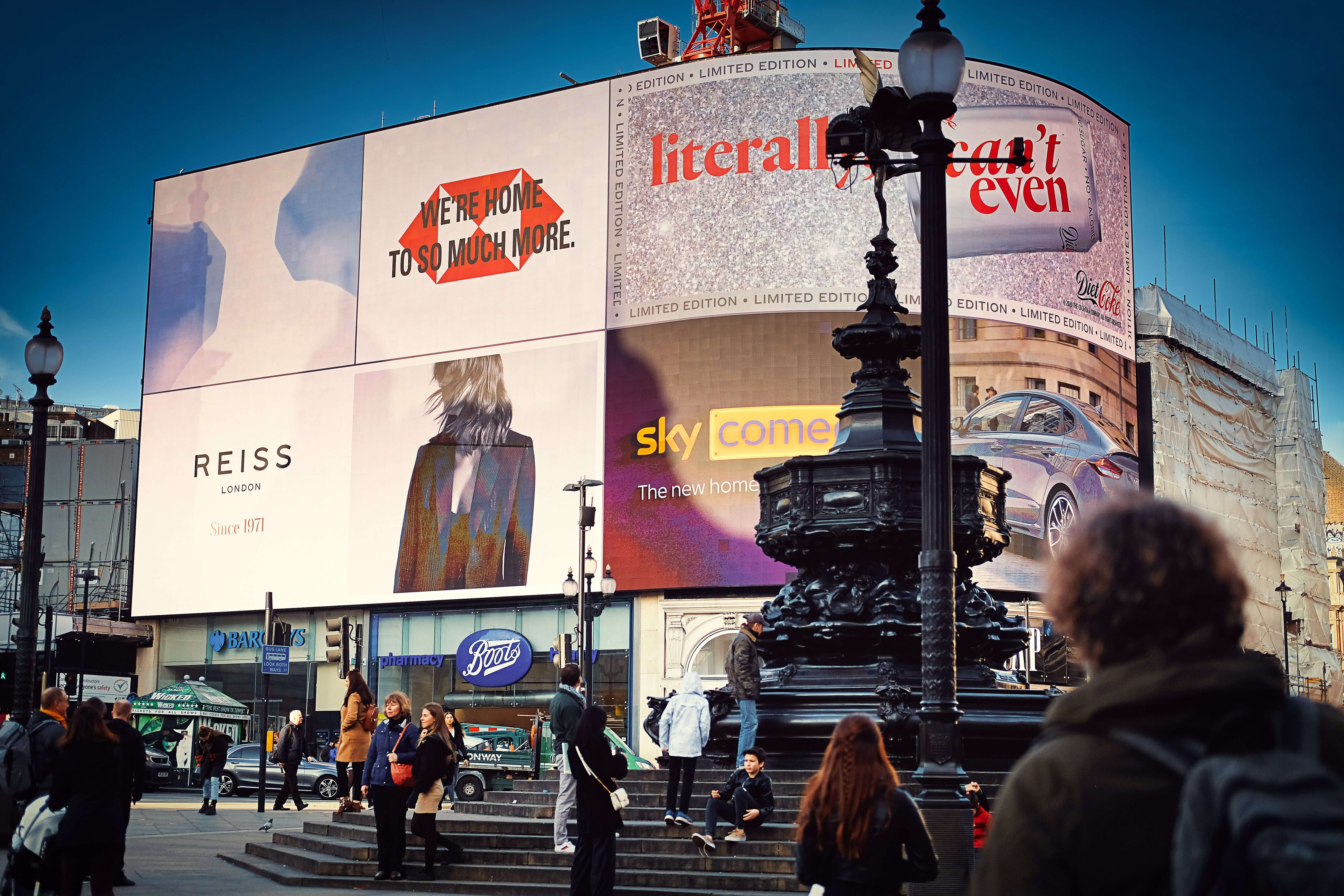 View of the famous giant advertising billboards and the Eros fountain at Piccadilly Circus in London, with passersby in the foreground.