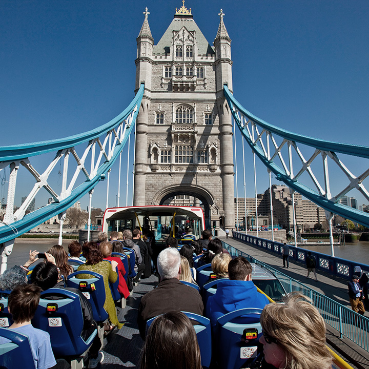 Vue depuis l'arrière des passagers assis à l'étage supérieur d'un bus décapotable traversant le Tower Bridge à Londres sous un ciel bleu.