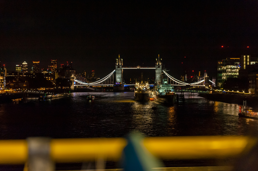 Vue nocturne du Tower Bridge illuminé au-dessus de la Tamise à Londres, prise depuis l'étage supérieur d'un bus décapotable au premier plan flou.