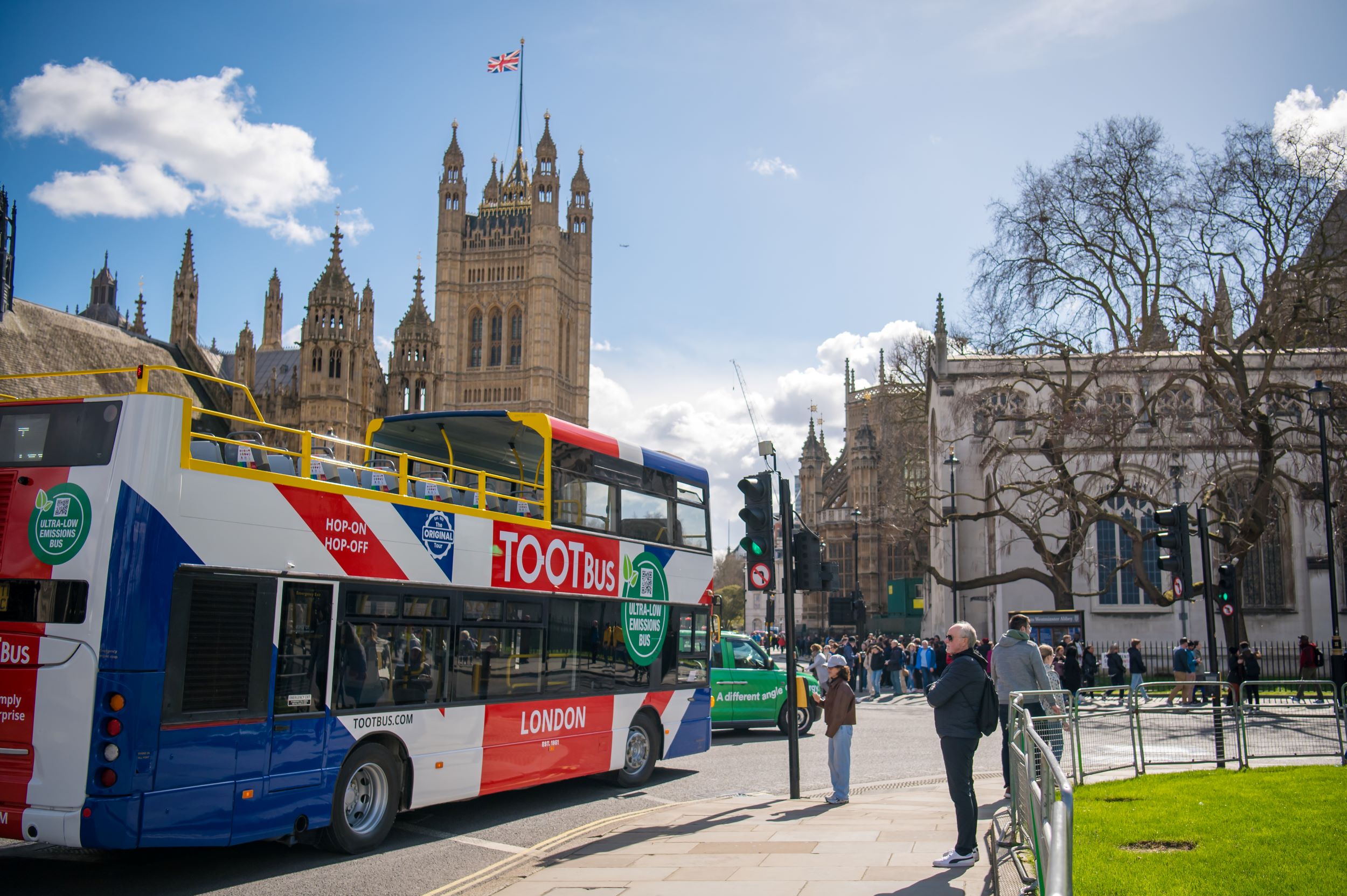 Un bus à impériale décapotable Tootbus bleu, blanc et rouge circulant à Londres près du Palais de Westminster par une journée ensoleillée.