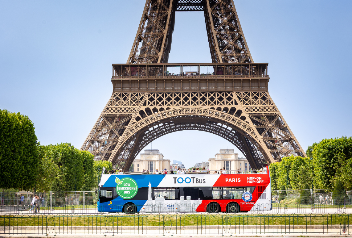 Eco-friendly Tootbus tour bus passing in front of the Eiffel Tower in Paris.