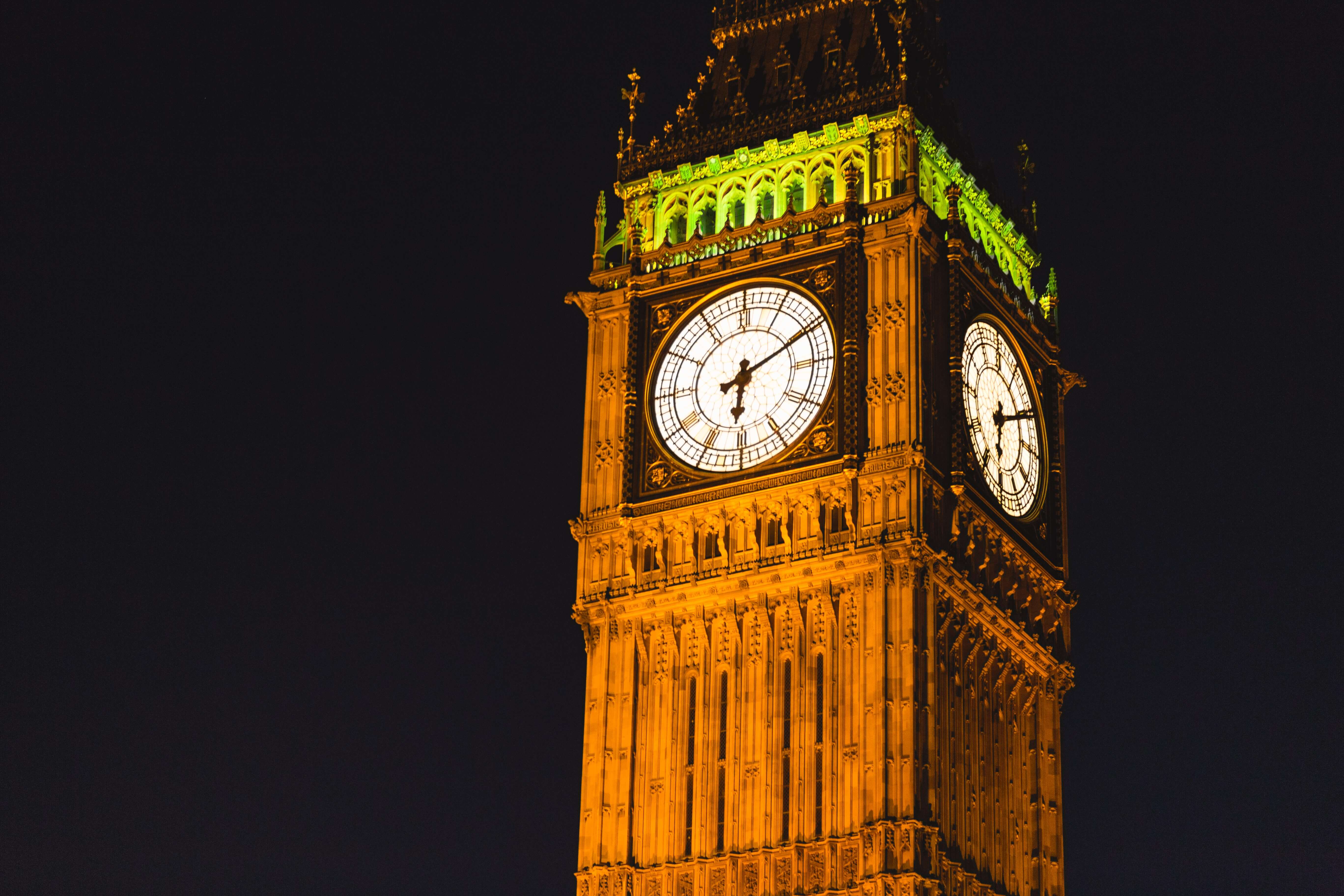 Gros plan nocturne sur les cadrans illuminés de la tour du Big Ben à Londres se détachant sur un ciel noir.