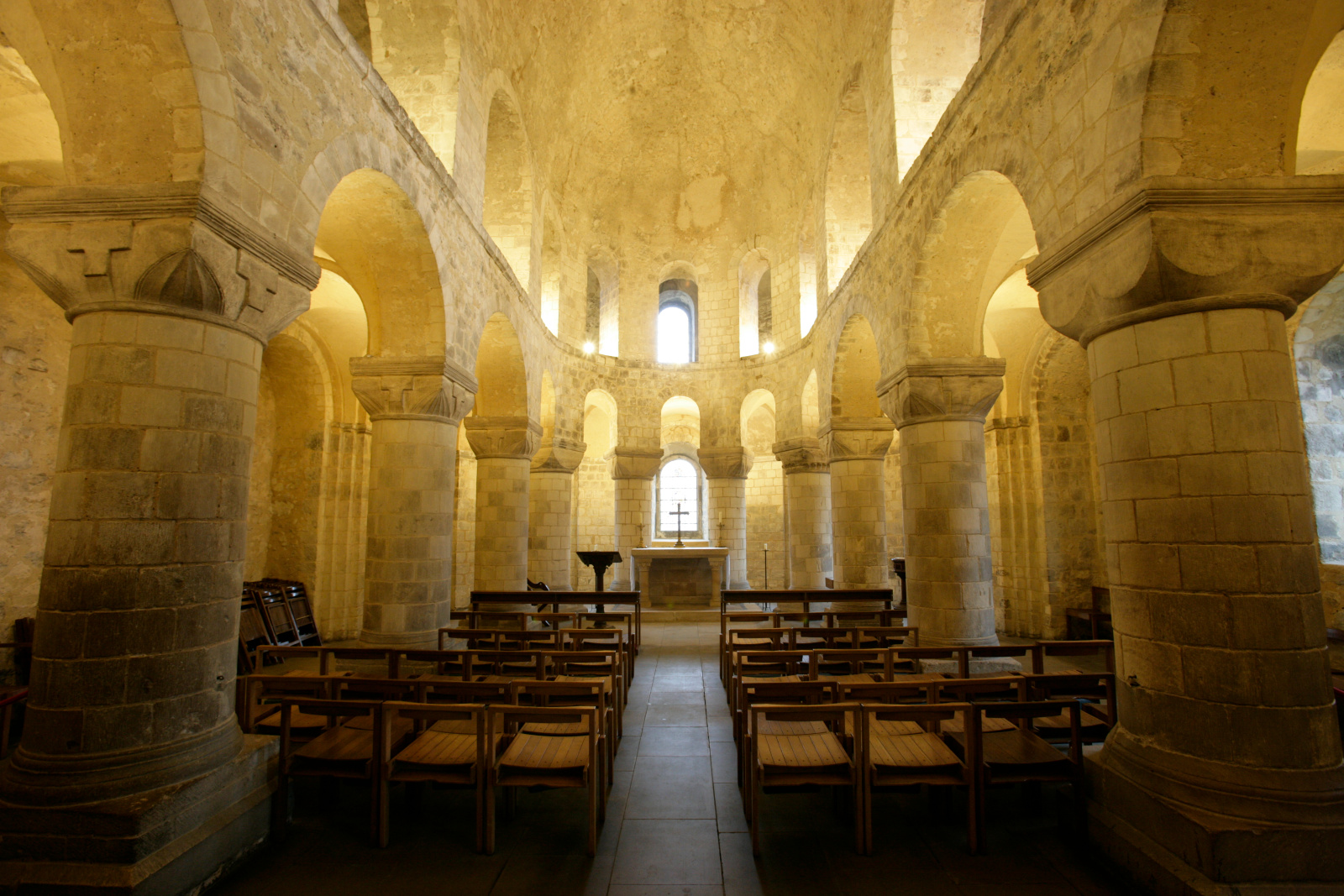 Vista del interior de la capilla de San Juan en la Torre de Londres, con pilares de piedra románicos, arcos de medio punto y filas de sillas.