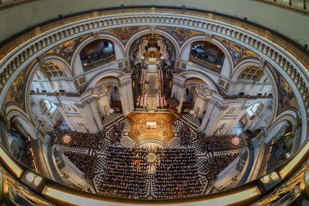 Wide-angle high-angle view from the dome's interior gallery of St Paul's Cathedral in London, showing the nave filled with visitors and congregation.
