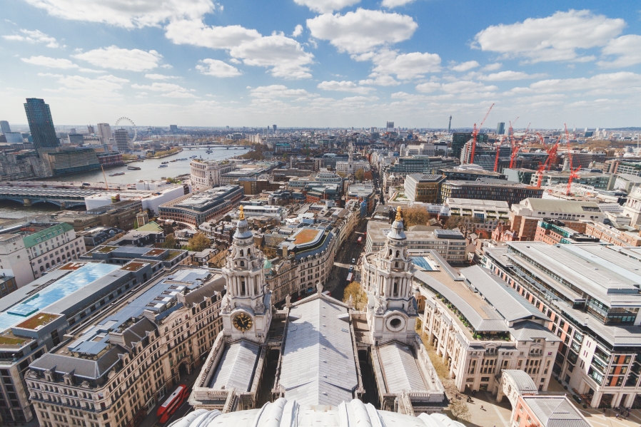 Aerial panoramic view of London from the top of St Paul's Cathedral, showing the River Thames, the London Eye, and the city under a sunny sky.