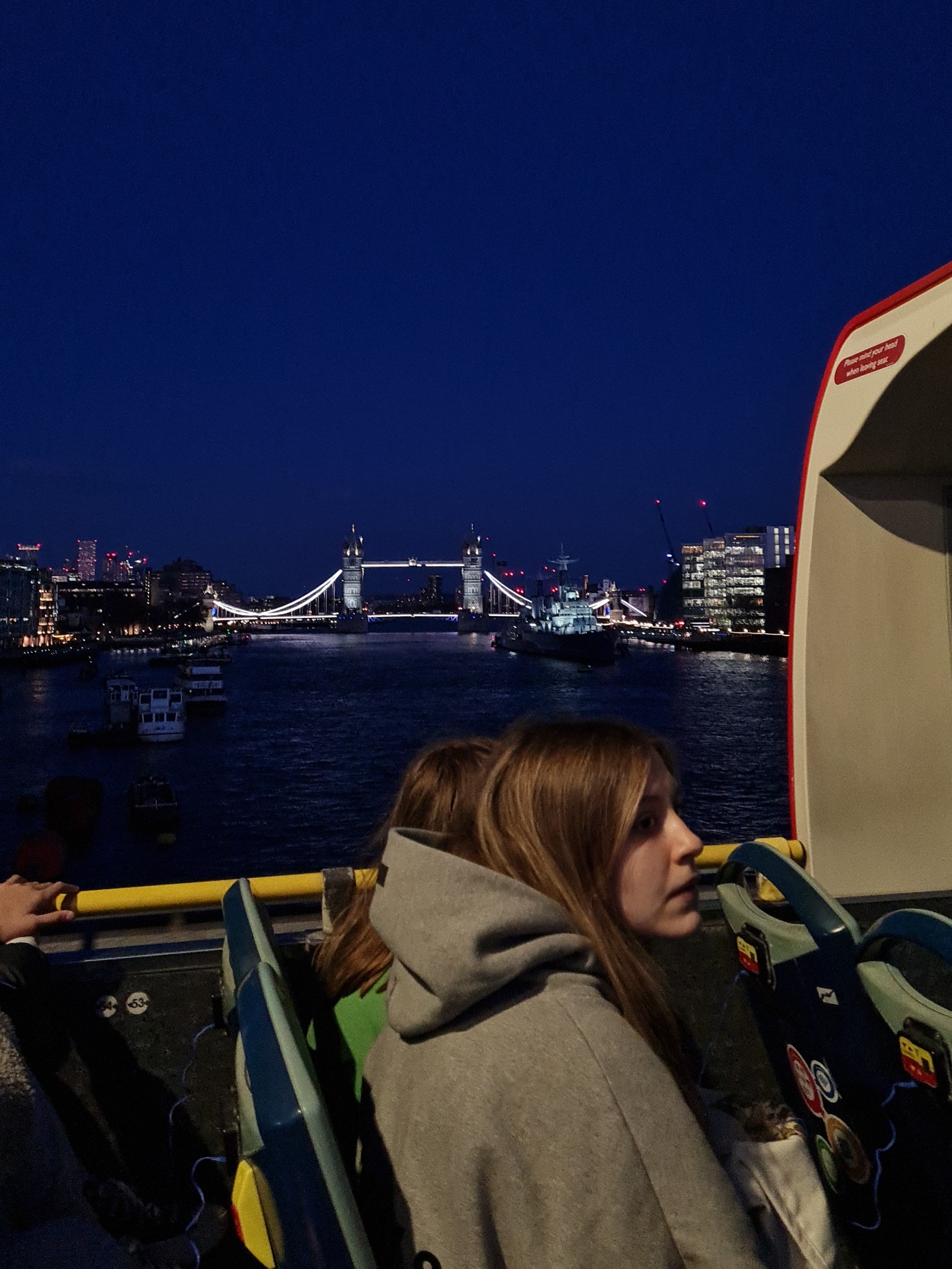 Des passagers assis à l'étage supérieur d'un Tootbus observant Tower Bridge illuminé au loin de nuit à Londres.