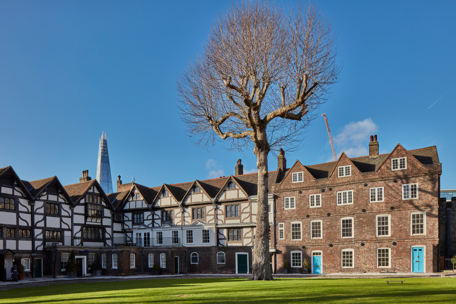 Edificios históricos de entramado de madera de la Queen's House en la Torre de Londres, con un gran árbol y el rascacielos The Shard al fondo.