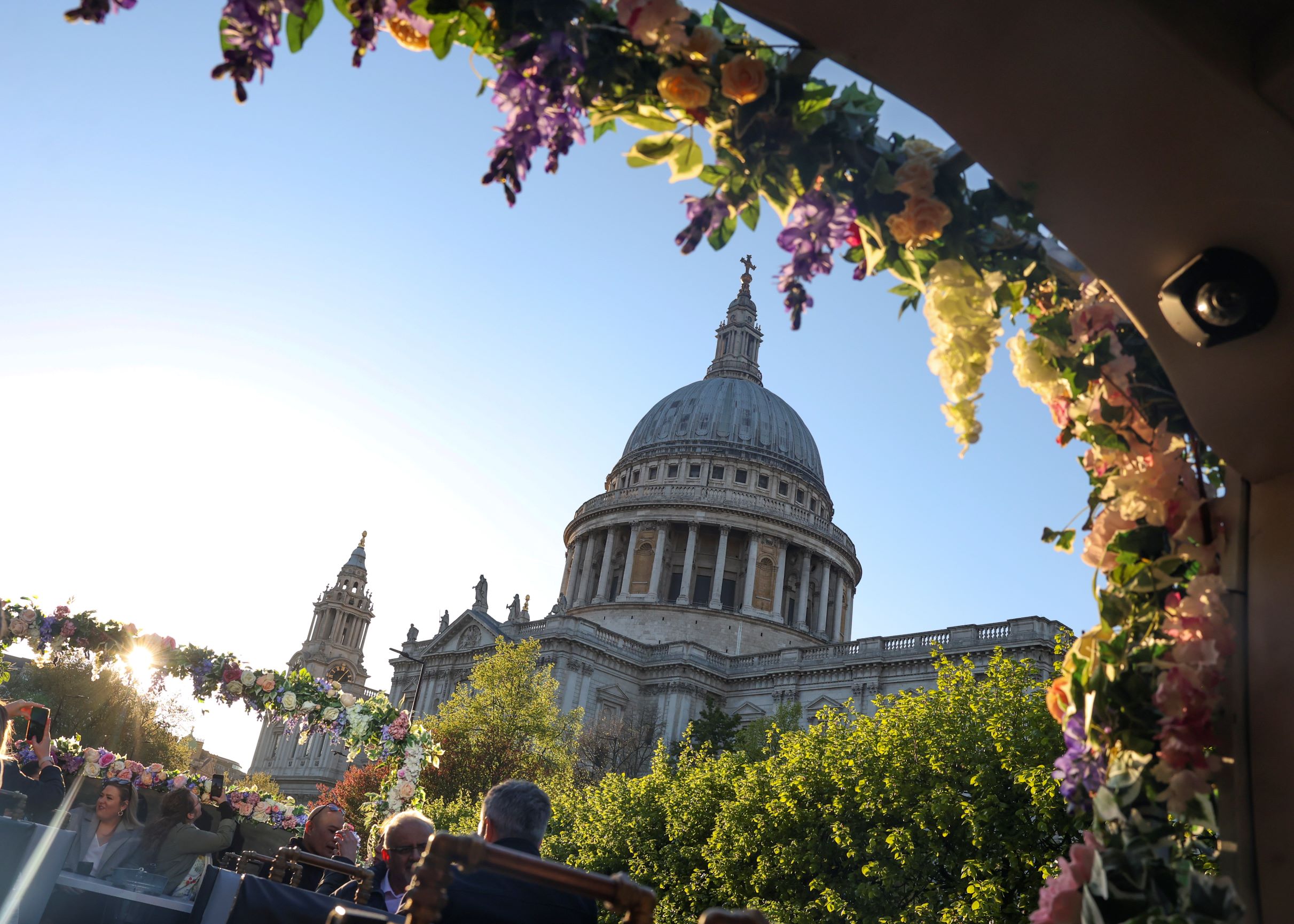 View of St Paul's Cathedral dome in London from an open-top bus framed by floral garlands.