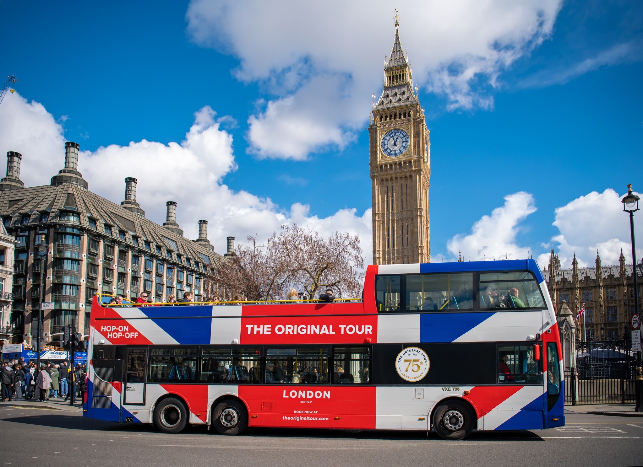 Un bus de "The Original Tour" passant devant Big Ben à Londres par une journée ensoleillée avec un ciel bleu.