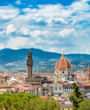 Veduta panoramica di Firenze con il Duomo, Palazzo Vecchio e cipressi sotto un cielo blu nuvoloso.