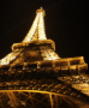 Low-angle close-up of the illuminated top of the Eiffel Tower glowing with golden light against the dark night sky in Paris.
