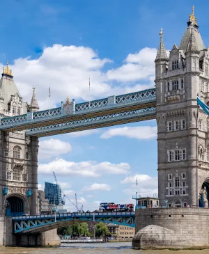 Iconic Tower Bridge suspension bridge in London with a Tootbus double-decker tourist bus crossing it under a blue sky with white clouds.